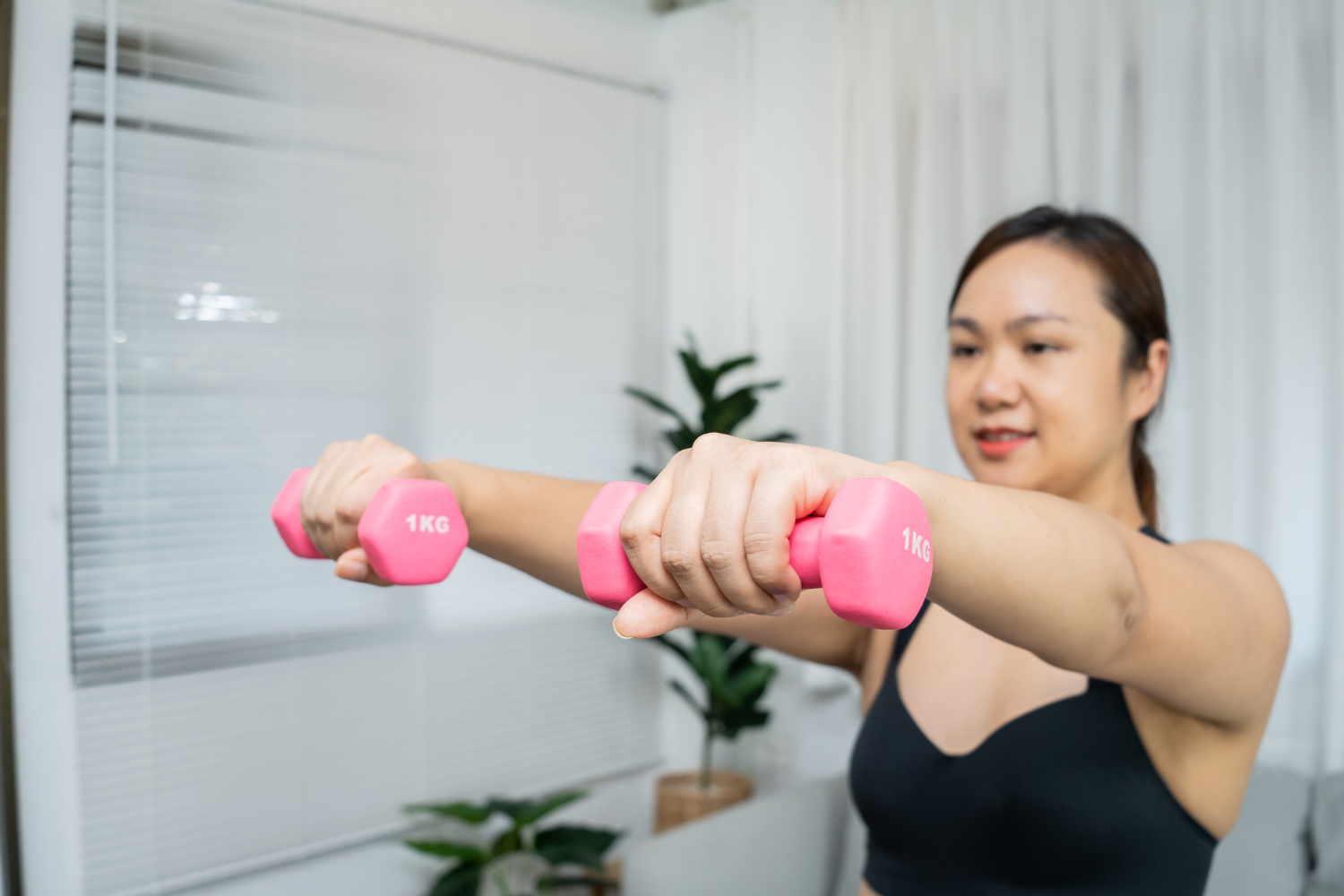 Woman lifting pink dumbbells during a home workout.